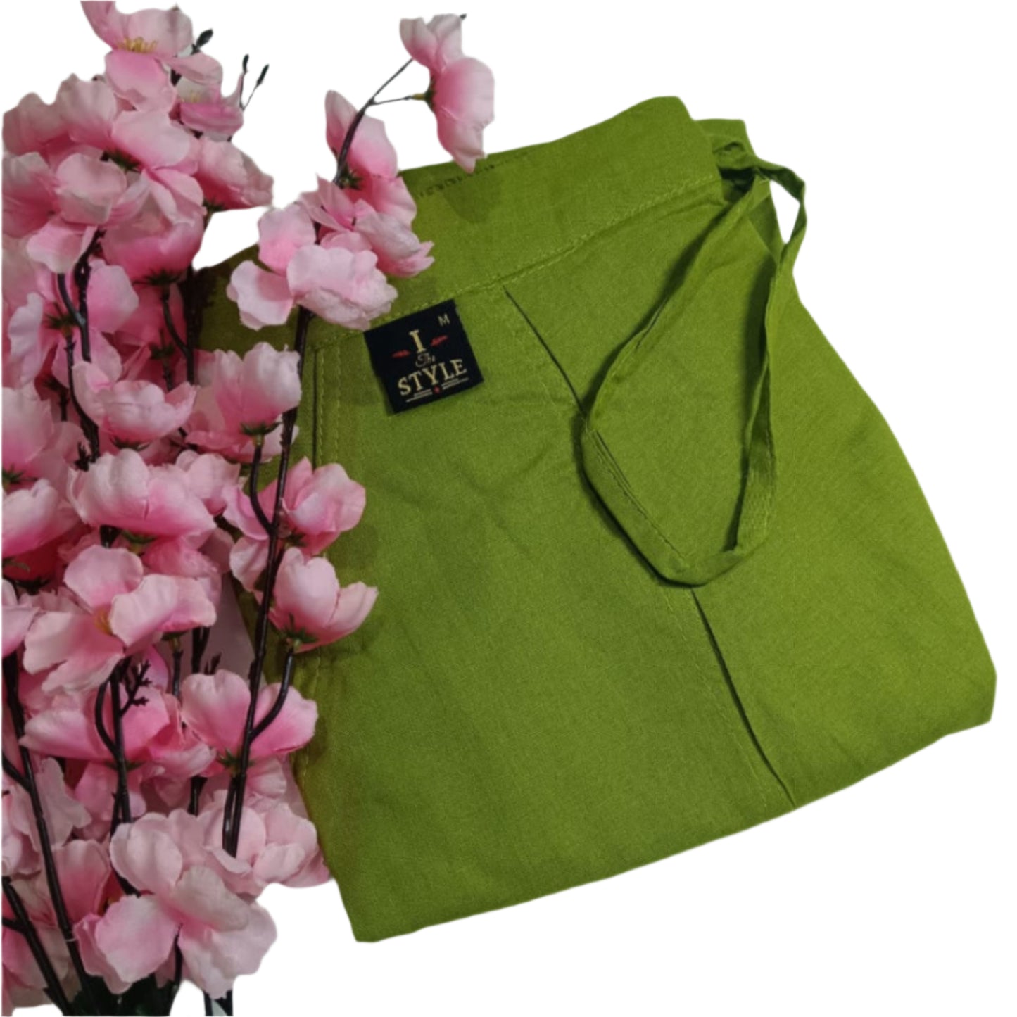 Green tote bag with a brand label next to pink flowers on a white background