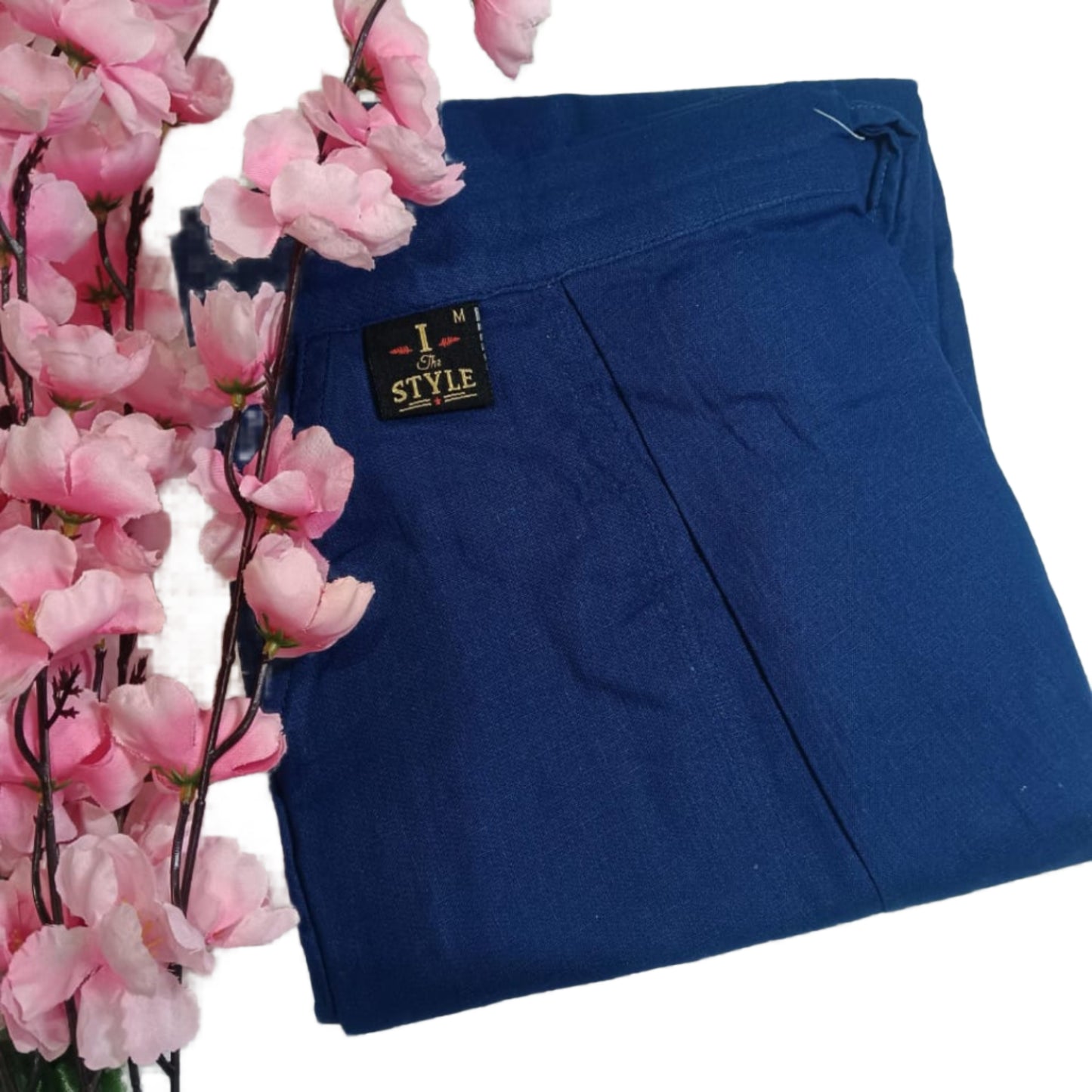 Blue pants with a brand label next to pink flowers on a white background