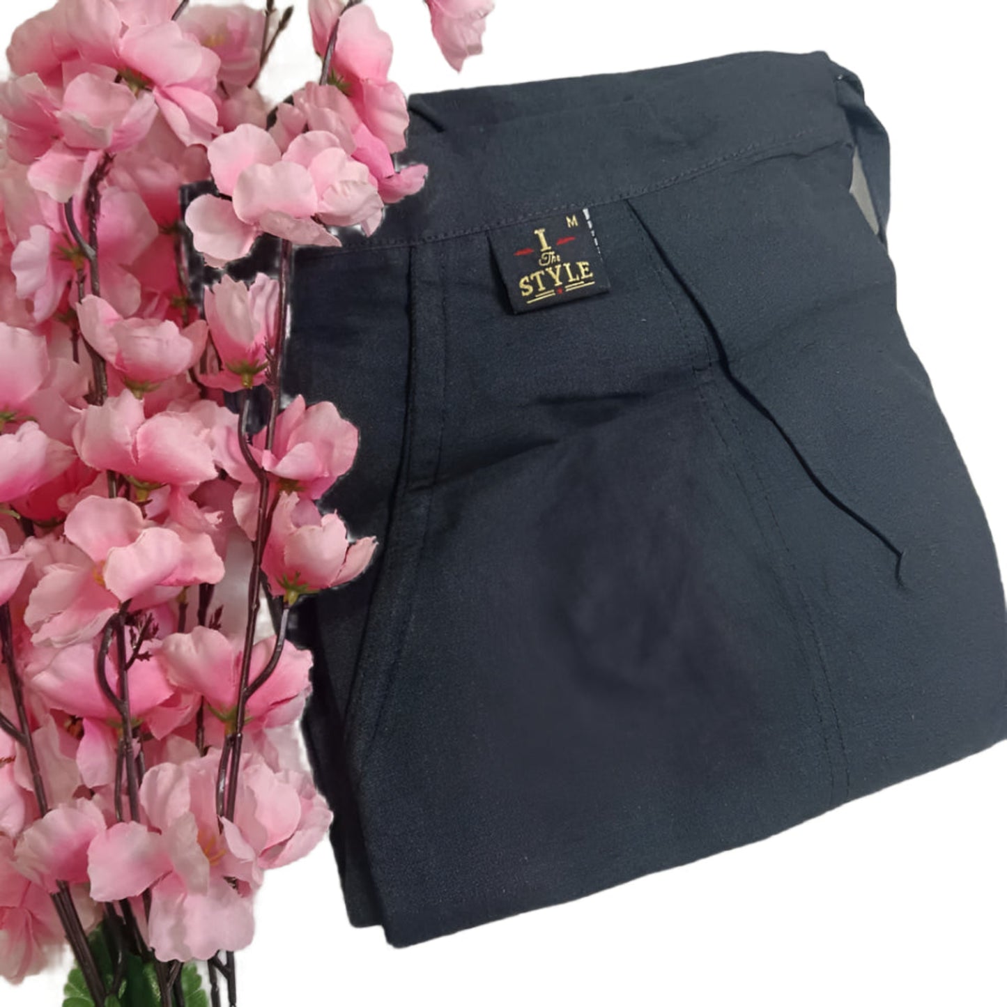 Black pants with a brand label next to pink flowers on a light background