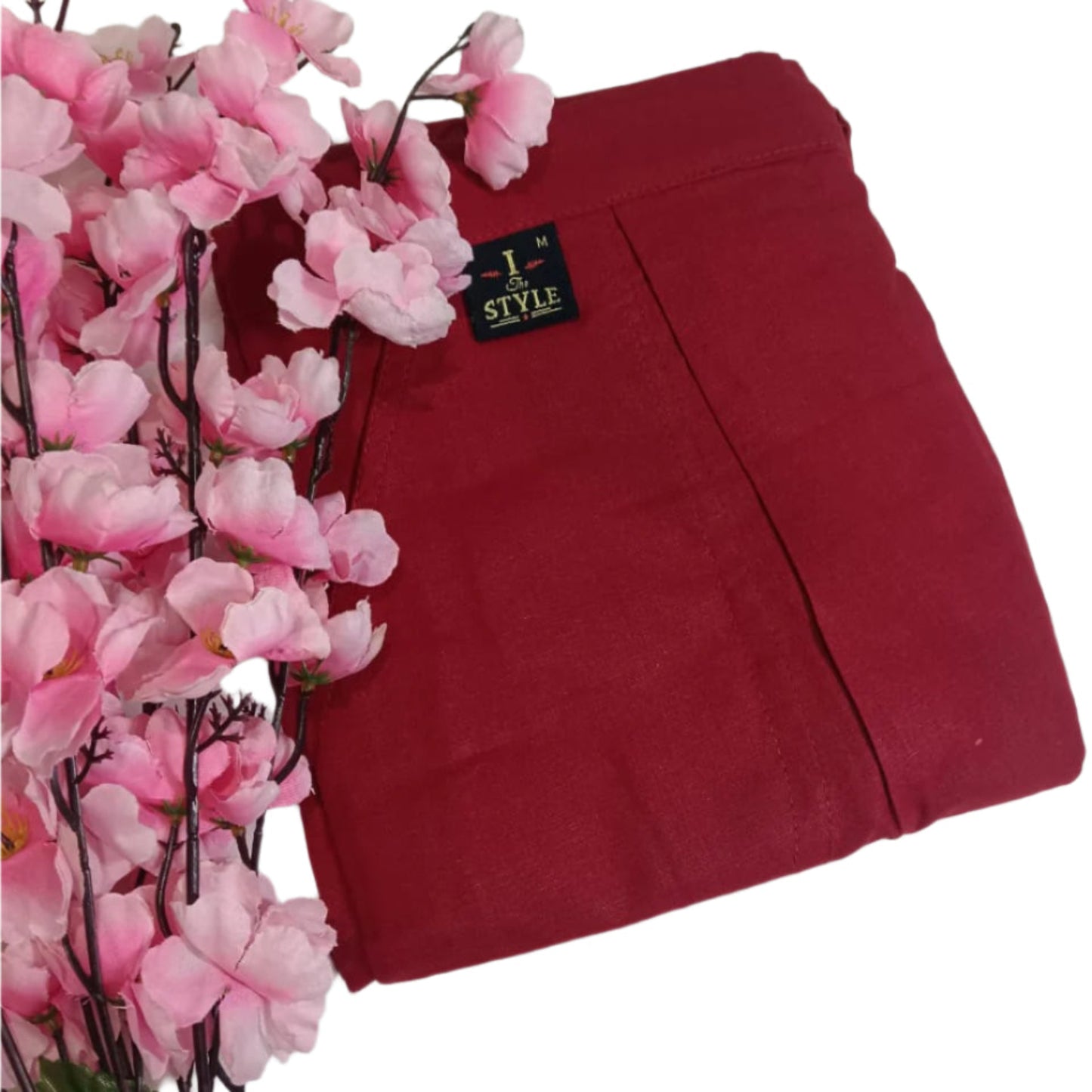 Red pants with a brand tag next to pink flowers on a white background